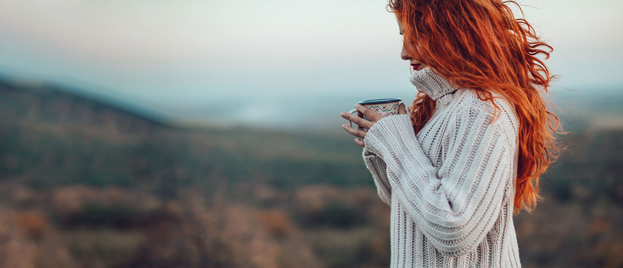 Young woman with bright red hair sipping a hot drink on a cold day outside