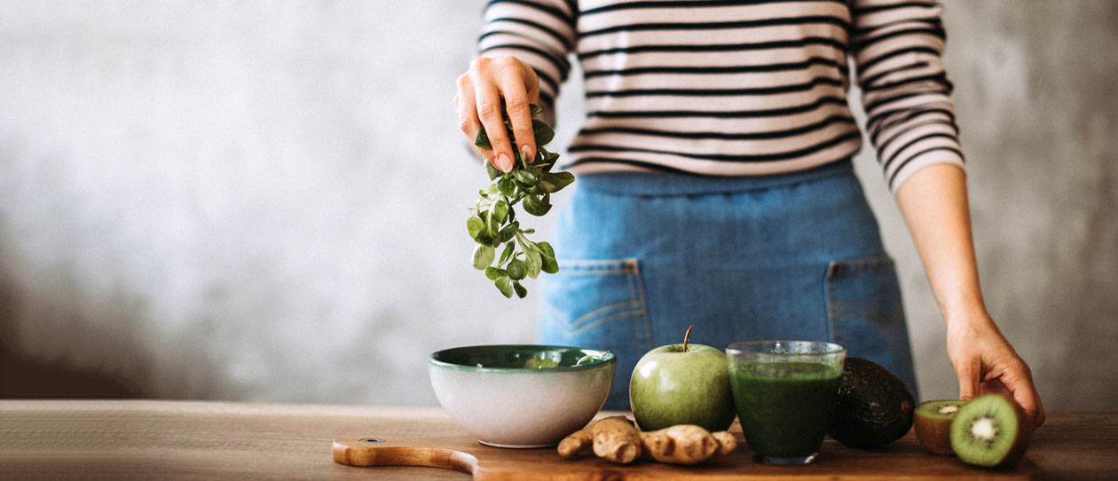 Woman preparing green smoothie at home on cutting board