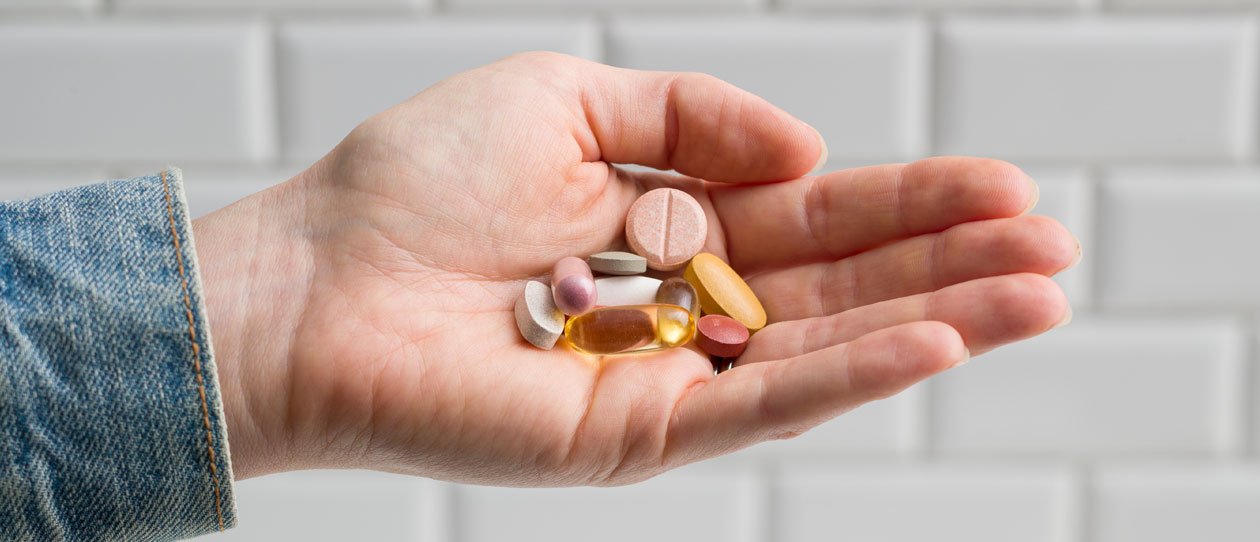 Close up image of a woman's hand holding a variety of vitamin supplements